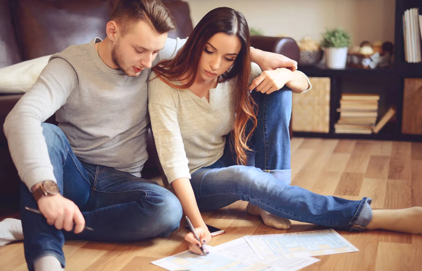 A couple sitting on the hardwood floor of their home looking at tax documents.