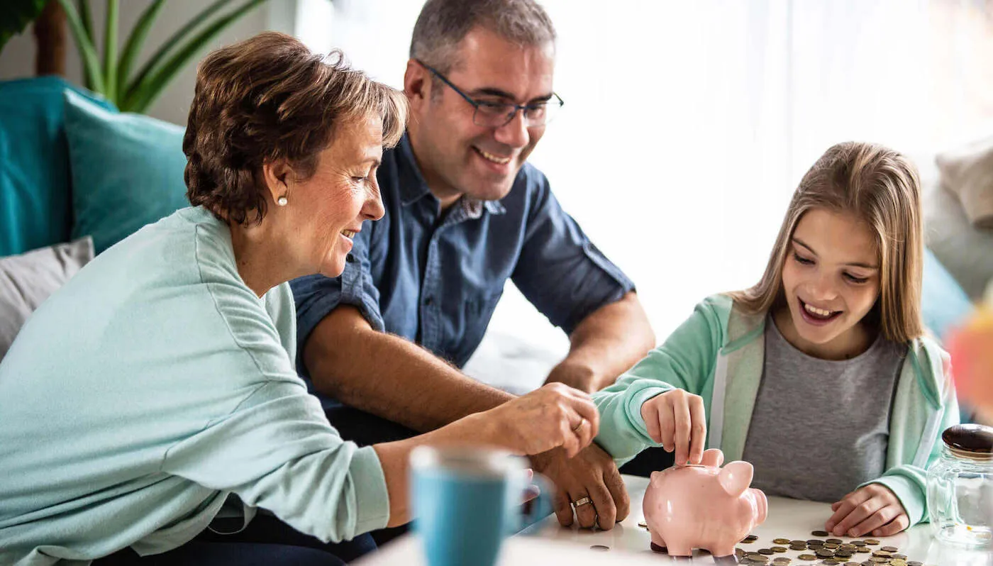 two females and one male of different generations gathered around the table putting coins in piggy bank