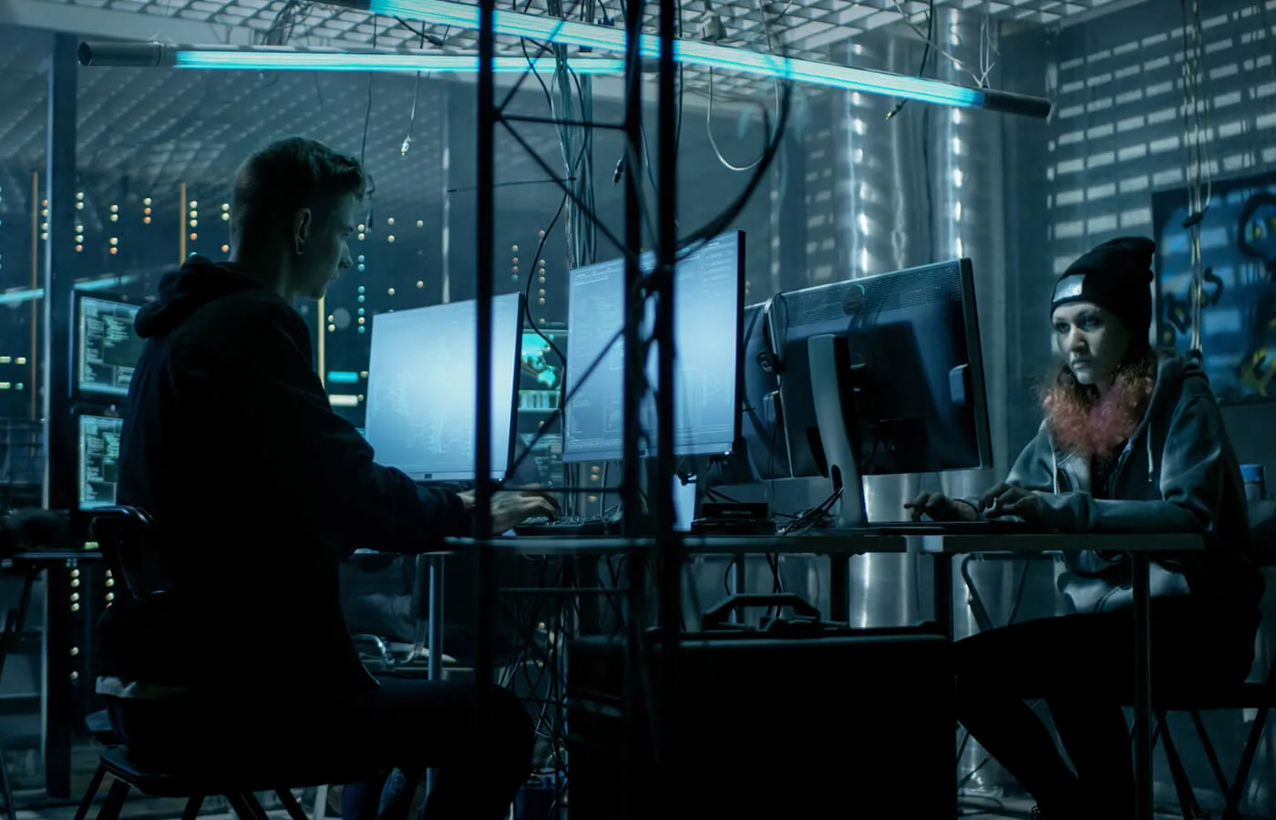 A man and a woman working on computers in a dark, industrial room.