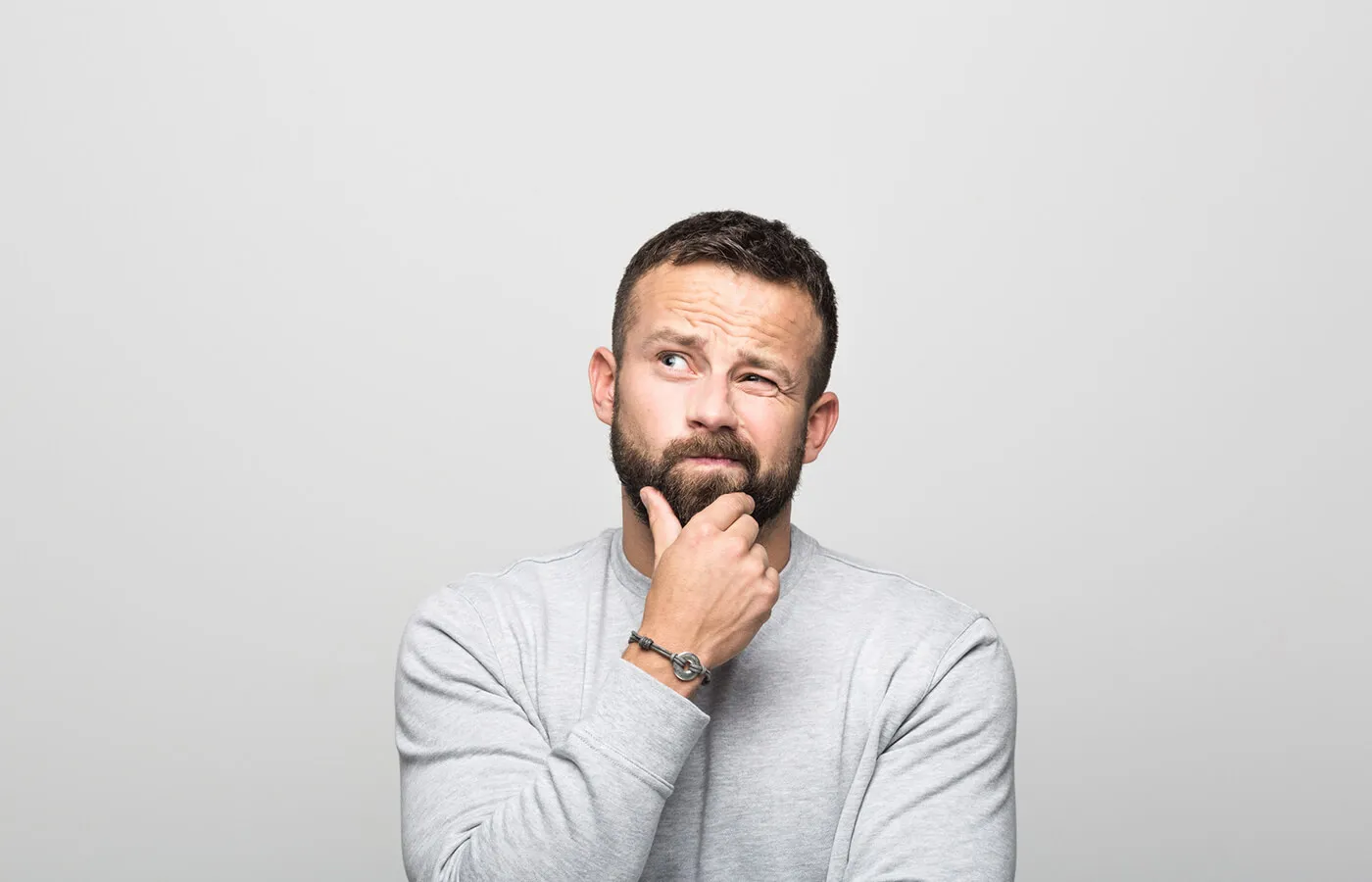 A pensive man stroking his beard and looking up at the ceiling