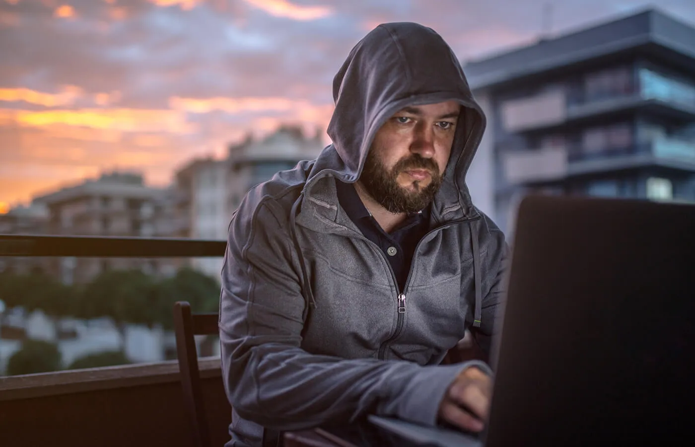 A hooded man using a laptop on a rooftop seating area.