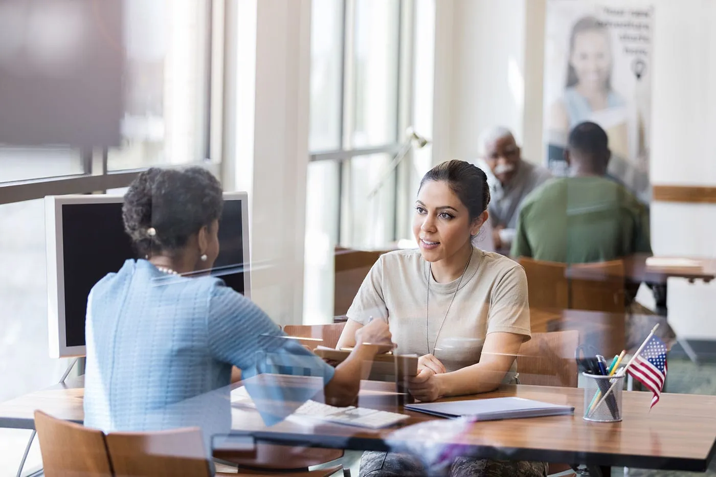 An agent talks with one her clients that is sitting across the table while she holds a document.