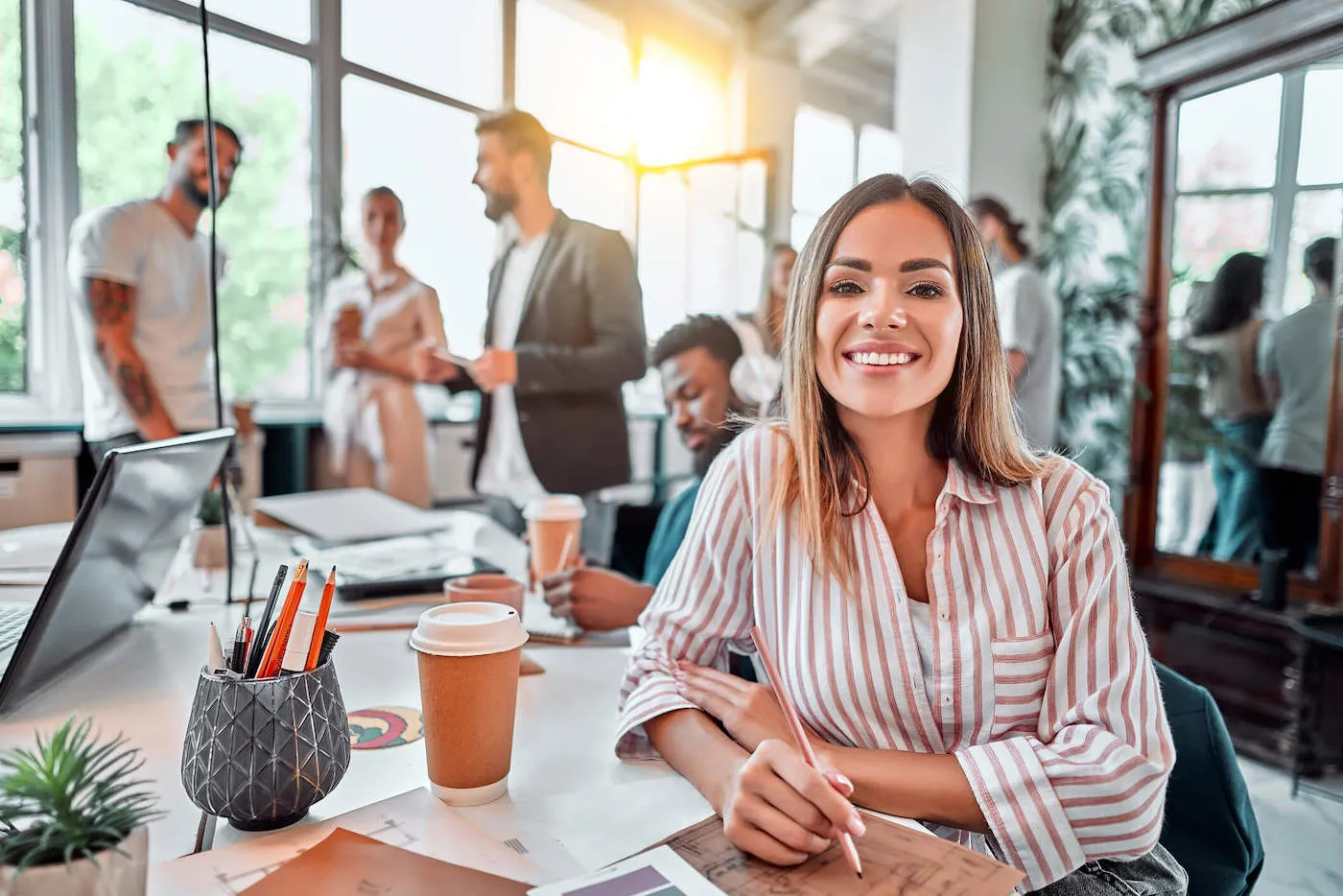 smiling woman with striped shirt sitting in a populated office space