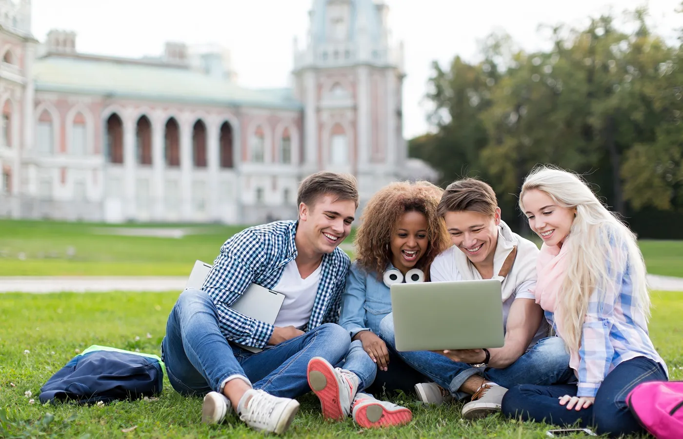 two males and two females seated on lawn looking at a laptop against a blurred background