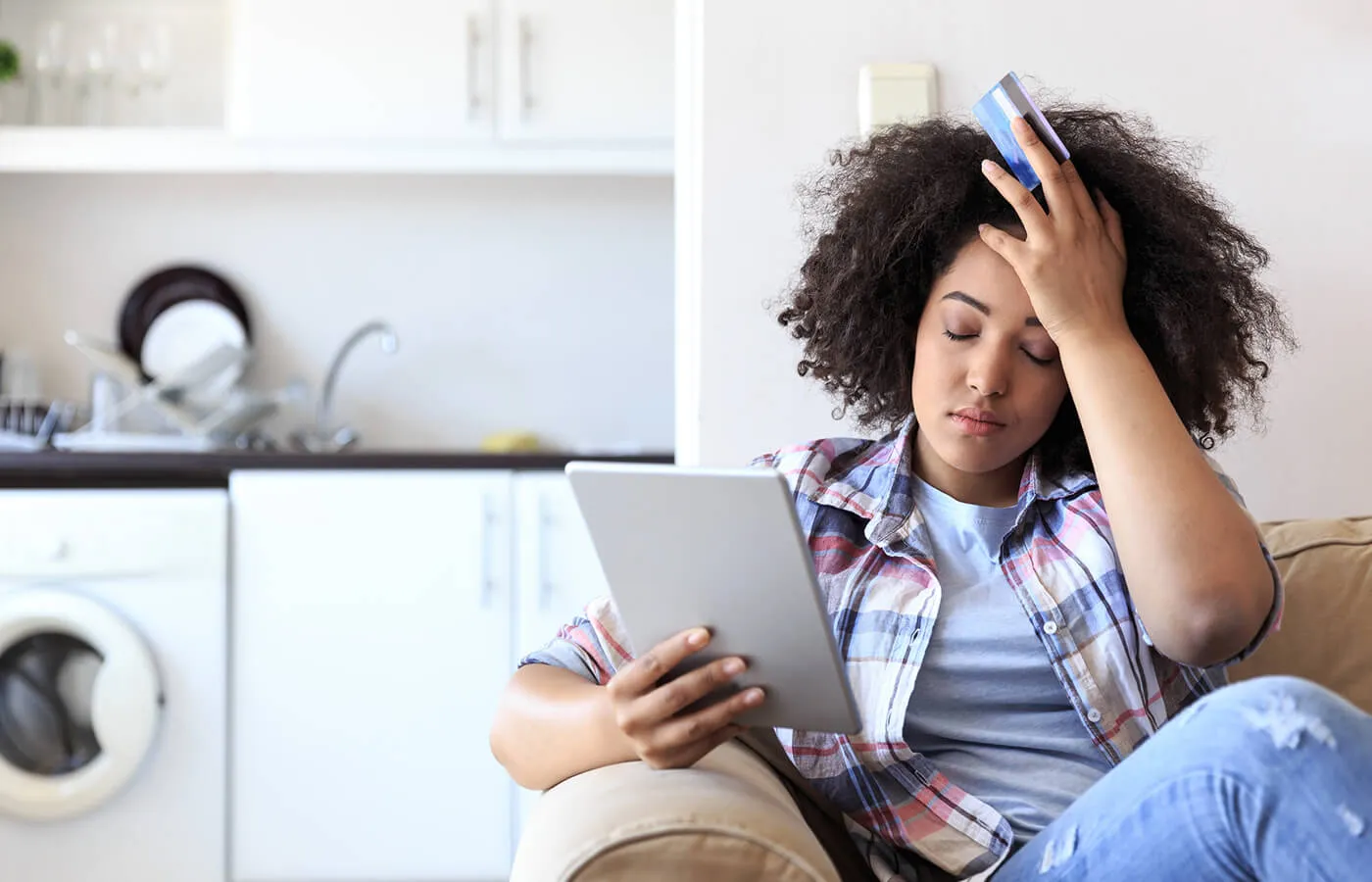 A woman looking mildly distressed while looking at her tablet and holding a credit card.