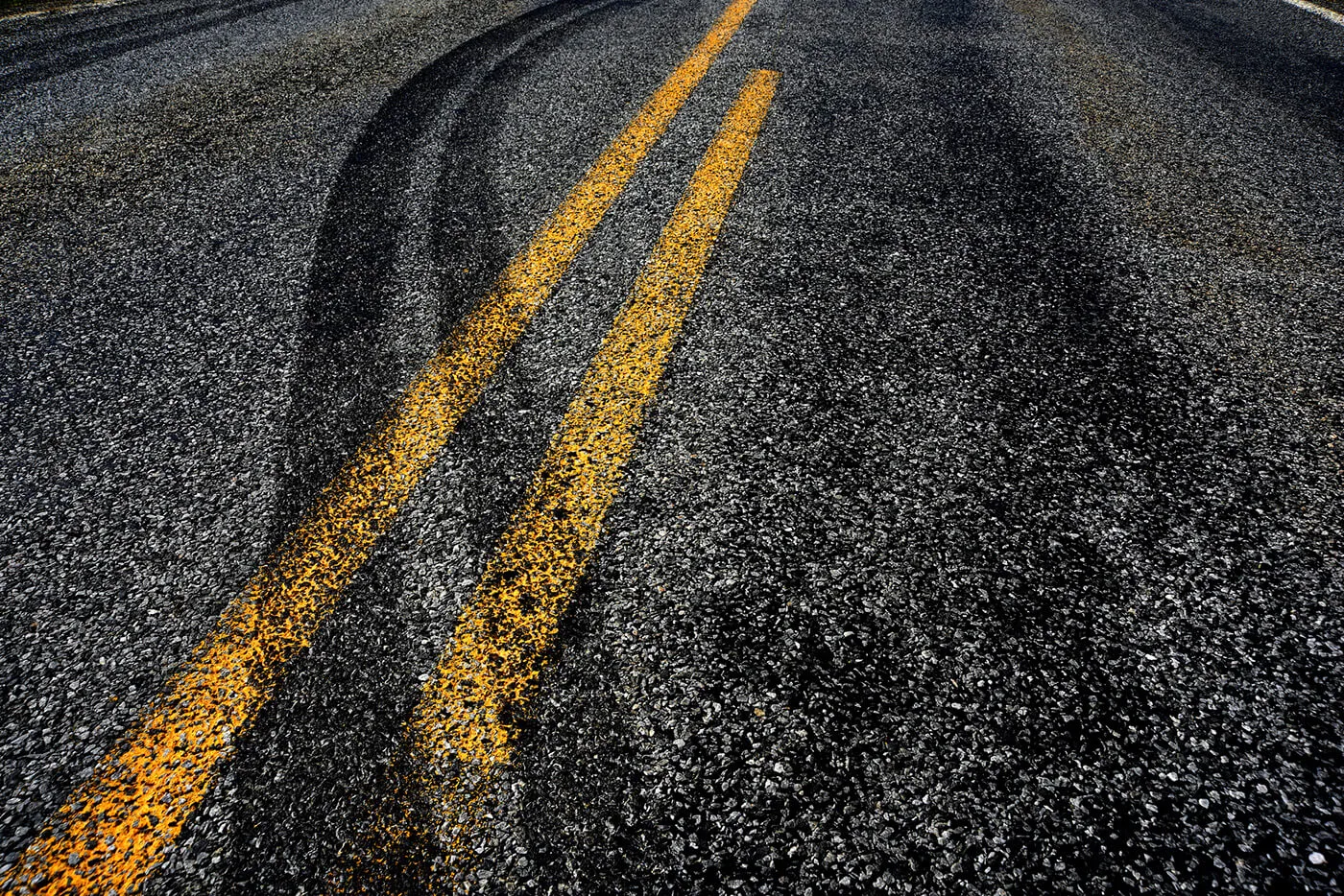 An asphalt road with tire tracks crossing the double yellow divider line.