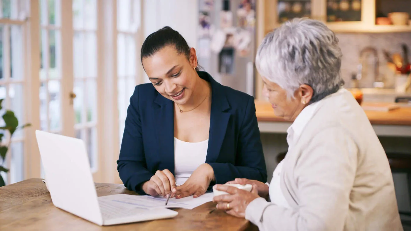 A woman wearing a suit discusses a document to an elderly woman next to her.