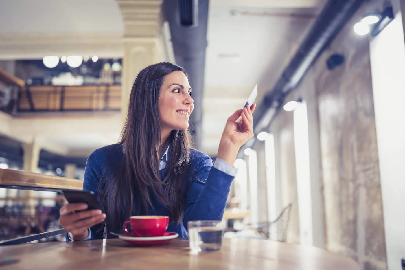 A woman holding her credit card smiles at a coffee shop.