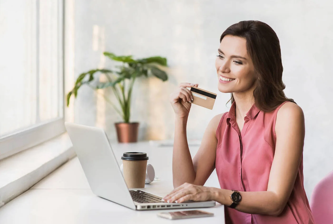 A woman hold her credit card while smiling at her computer while she holds her credit card.