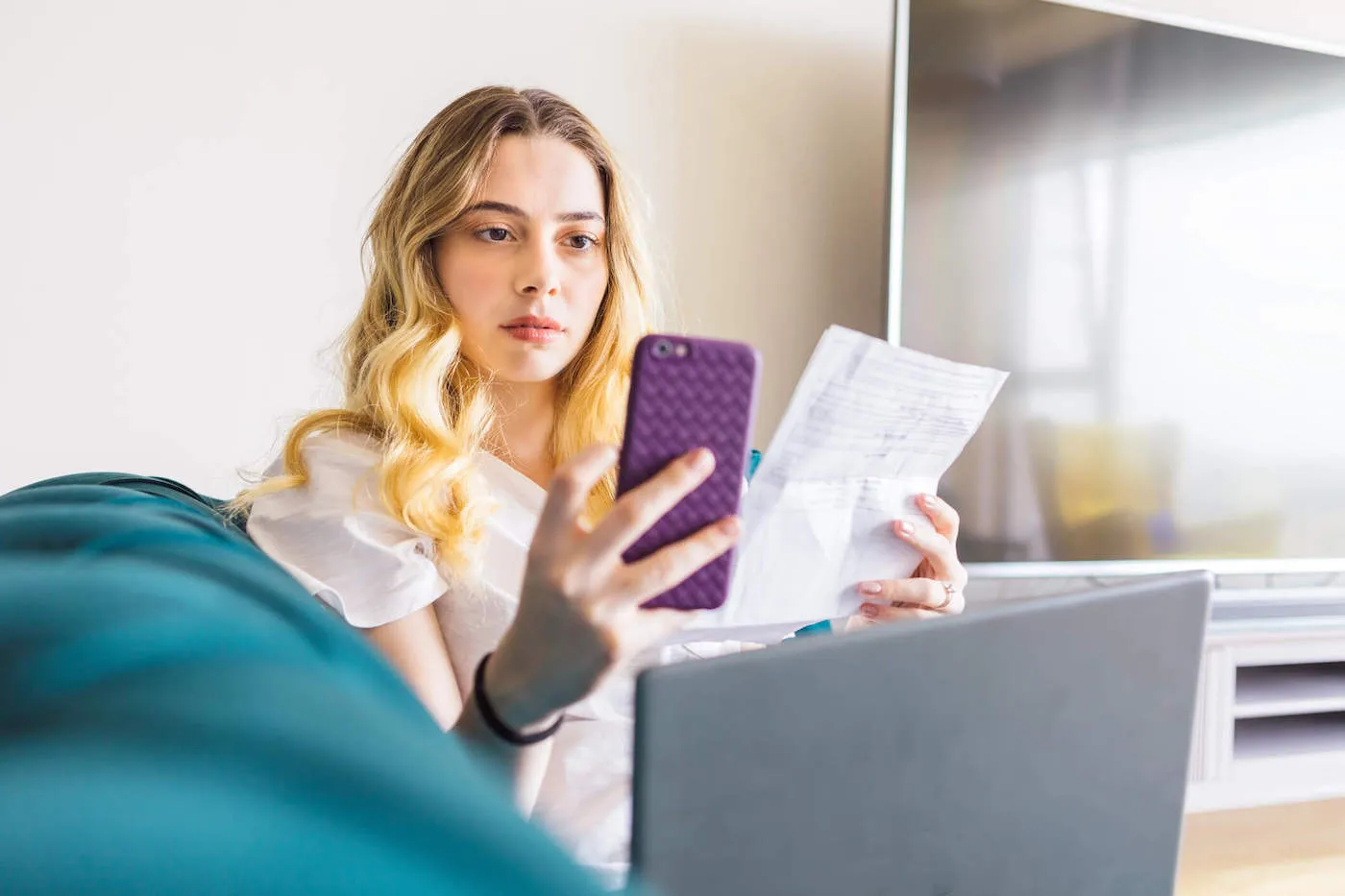 A young woman uses her purple colored phone while holding documents in her other hand.