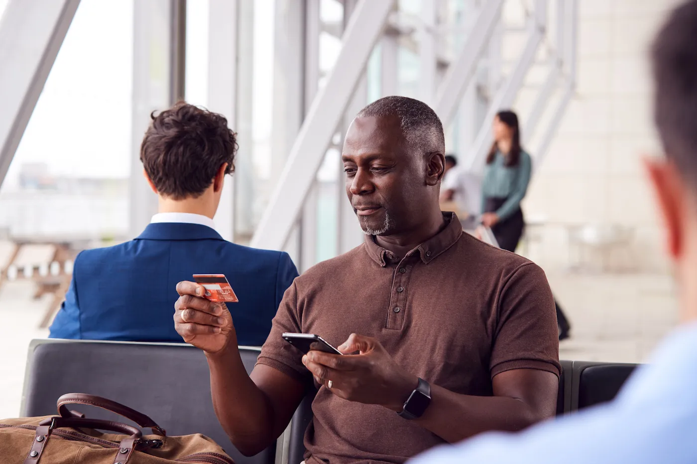 Businessman Sitting In Airport Departure Lounge Using Mobile Phone and Credit Card.