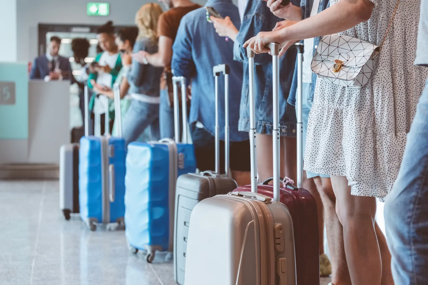 Travelers with luggage using smart phones while waiting in line for boarding at airport. Focus on wheeled luggage.