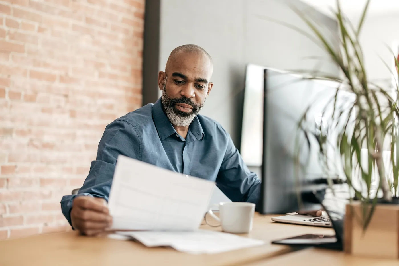 Man sitting at desk and reading papers next to his laptop.