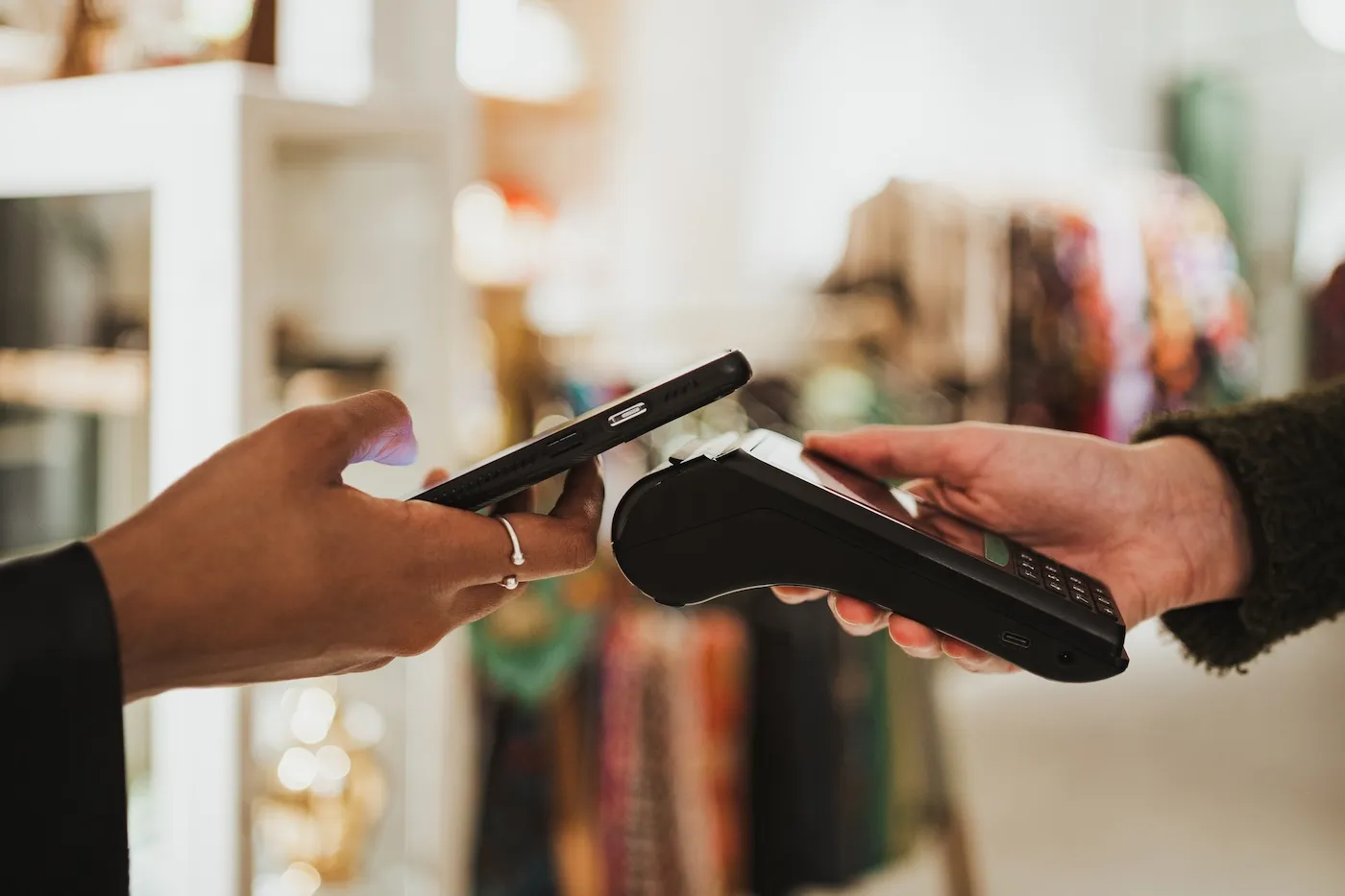 Close up shot of a woman paying contactless on a POS in a shop. She is using her phone.