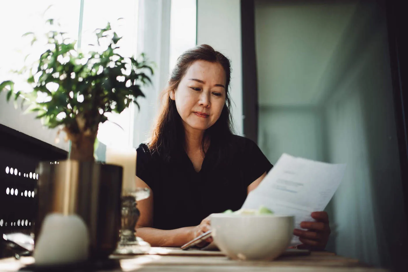 Asian woman in black shirt looking at personal cash flow statement paper.