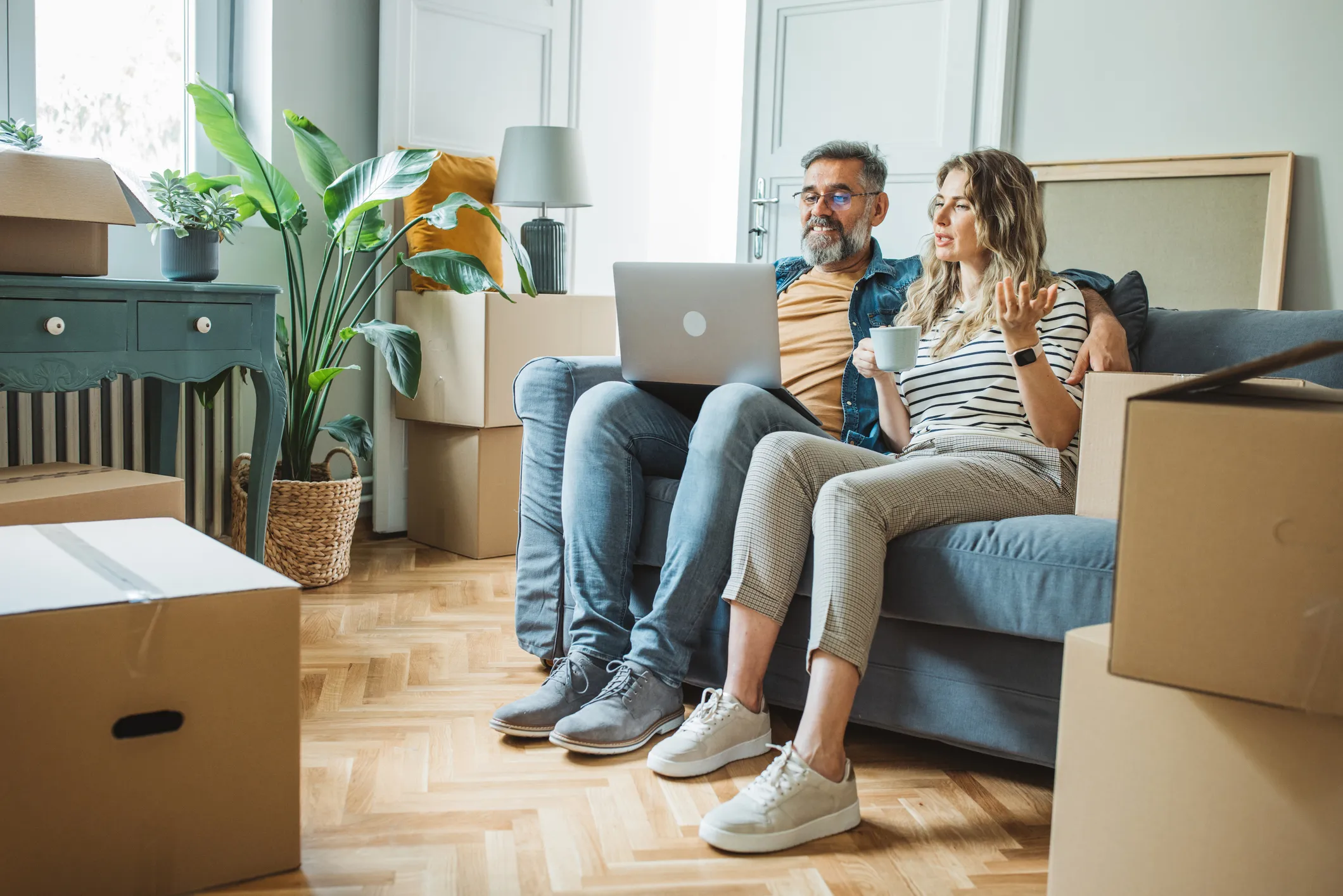 Mature couple moves in to their new home, they are using laptop to buy stuff for new house and enjoying the time together.