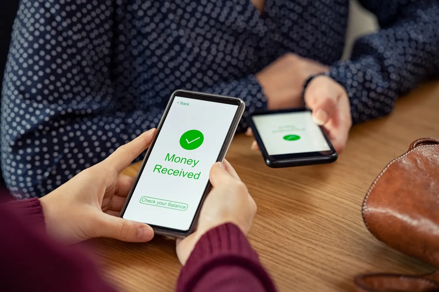 Close up of two friends' hands holding two mobile phones with a peer-to-peer payment app open.