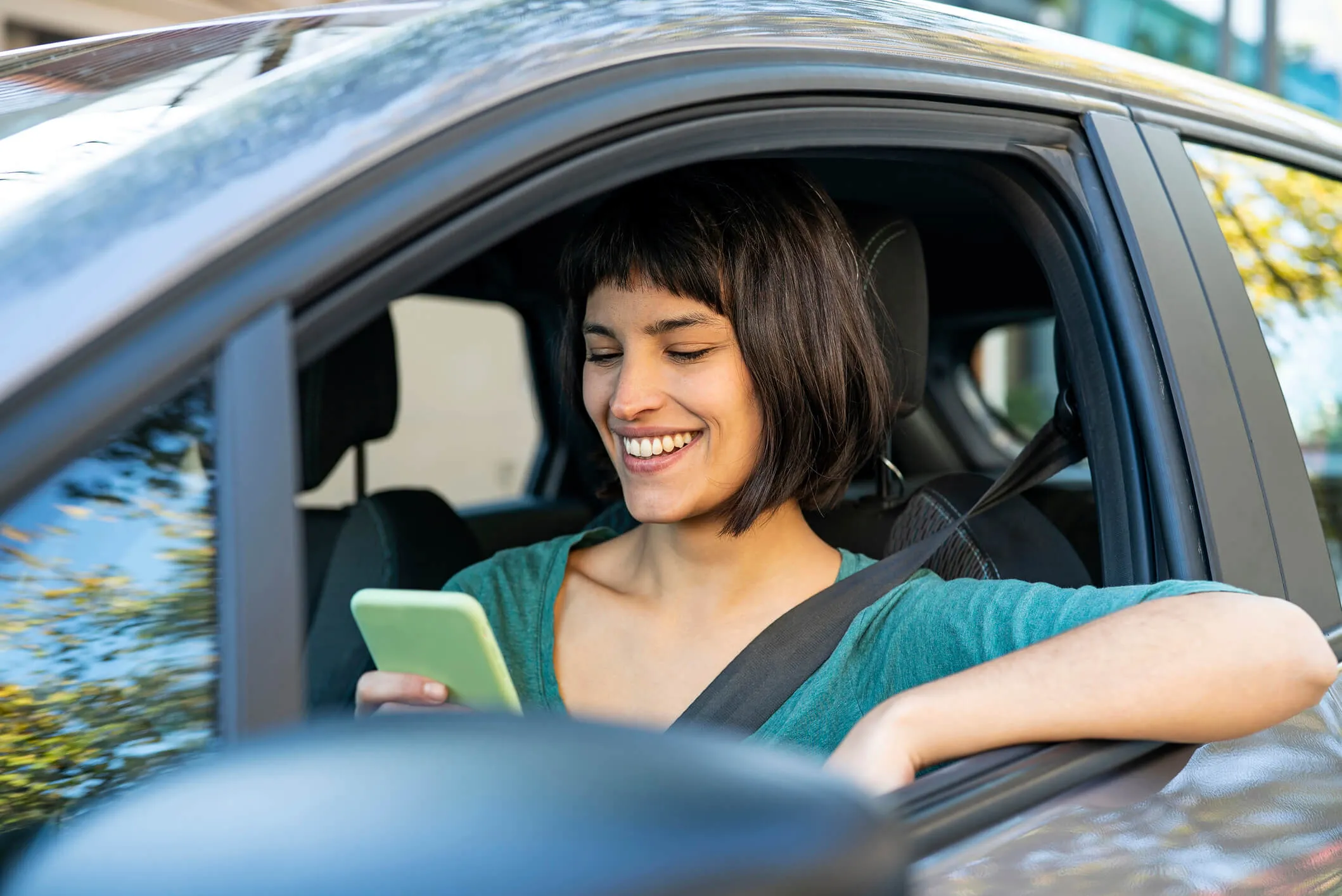 Smiling woman using mobile phone while sitting in driver's seat in the car