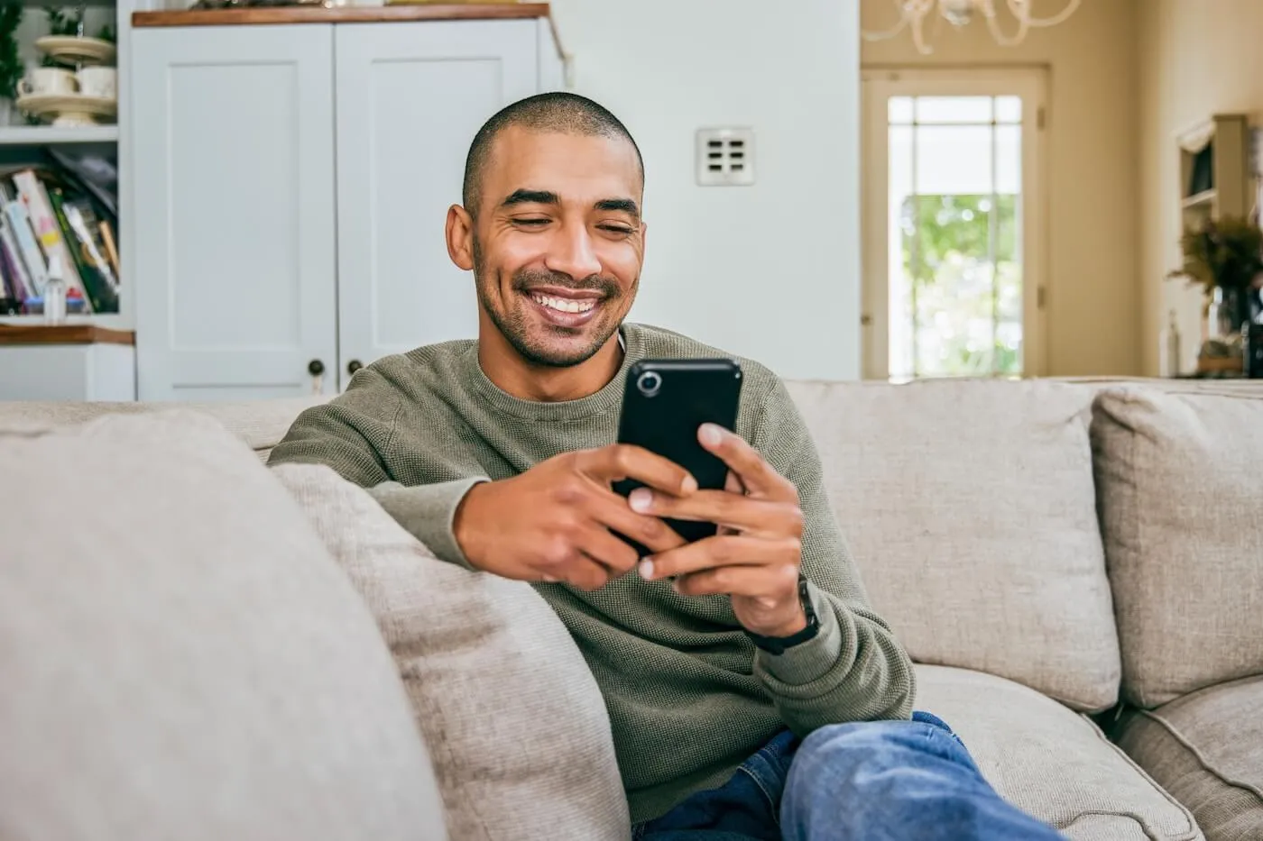 Smiling man using his smartphone while sitting on a couch