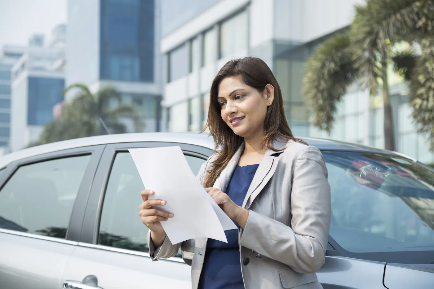 A woman reading a paper about the book value of her car, standing next to her car.