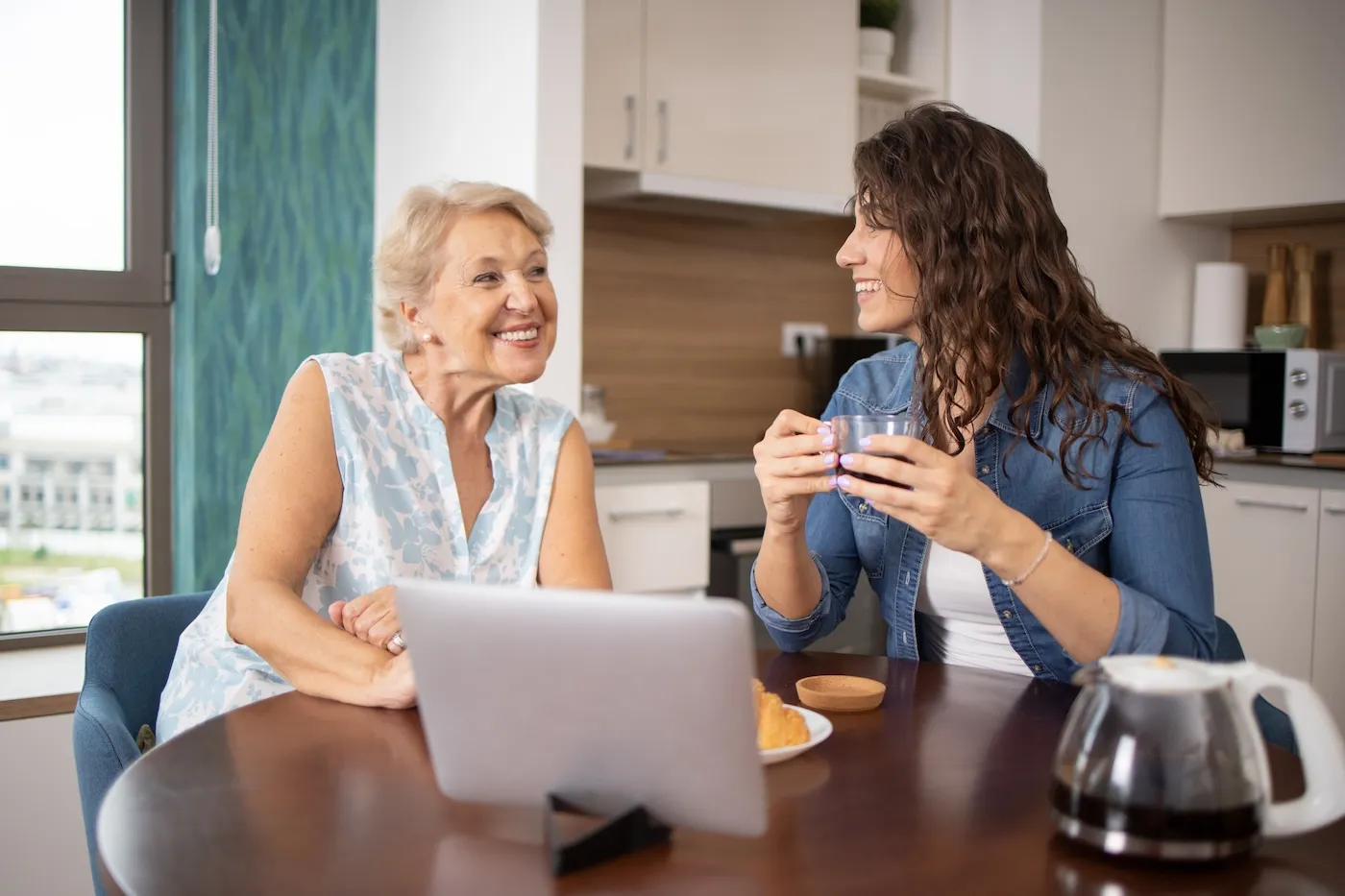 Two women sitting together with a laptop at a kitchen table.