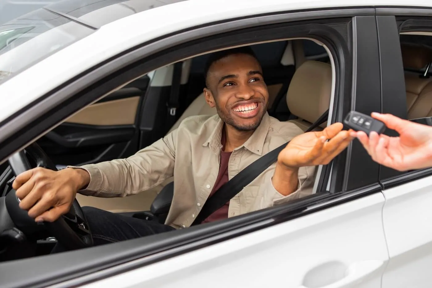 Smiling man sitting in the car and taking car keys from the dealership agent