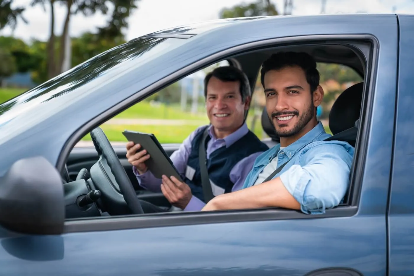 Smiling young man passing a driving test with a male instructor on a passenger seat