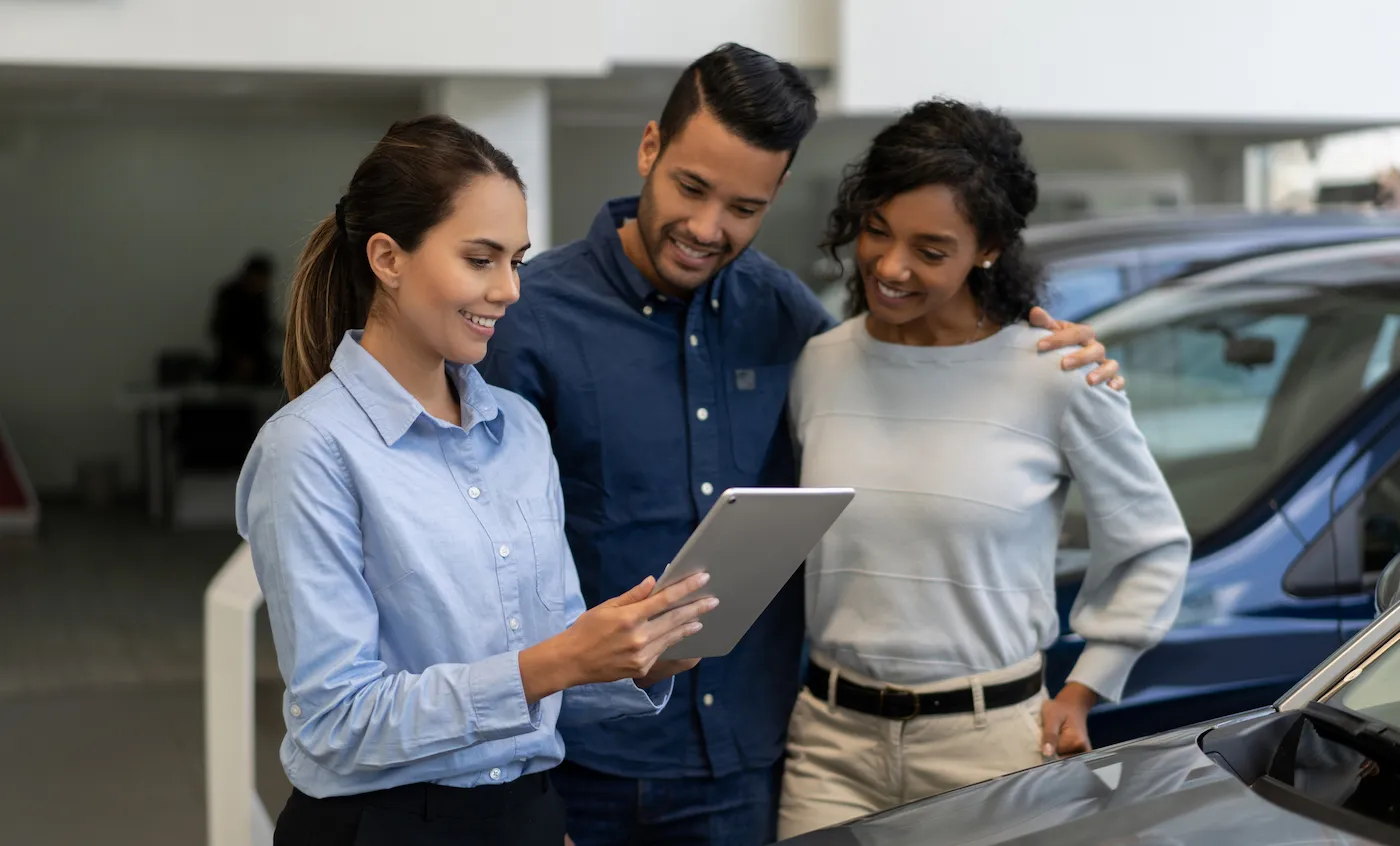 Portrait of a saleswoman at a car dealership talking to a happy couple and showing them info on a tablet computer