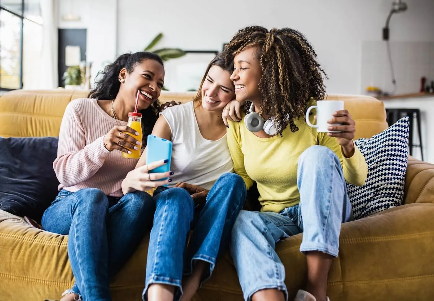 Three laughing college girls sitting on the couch with drinks while making a selfie