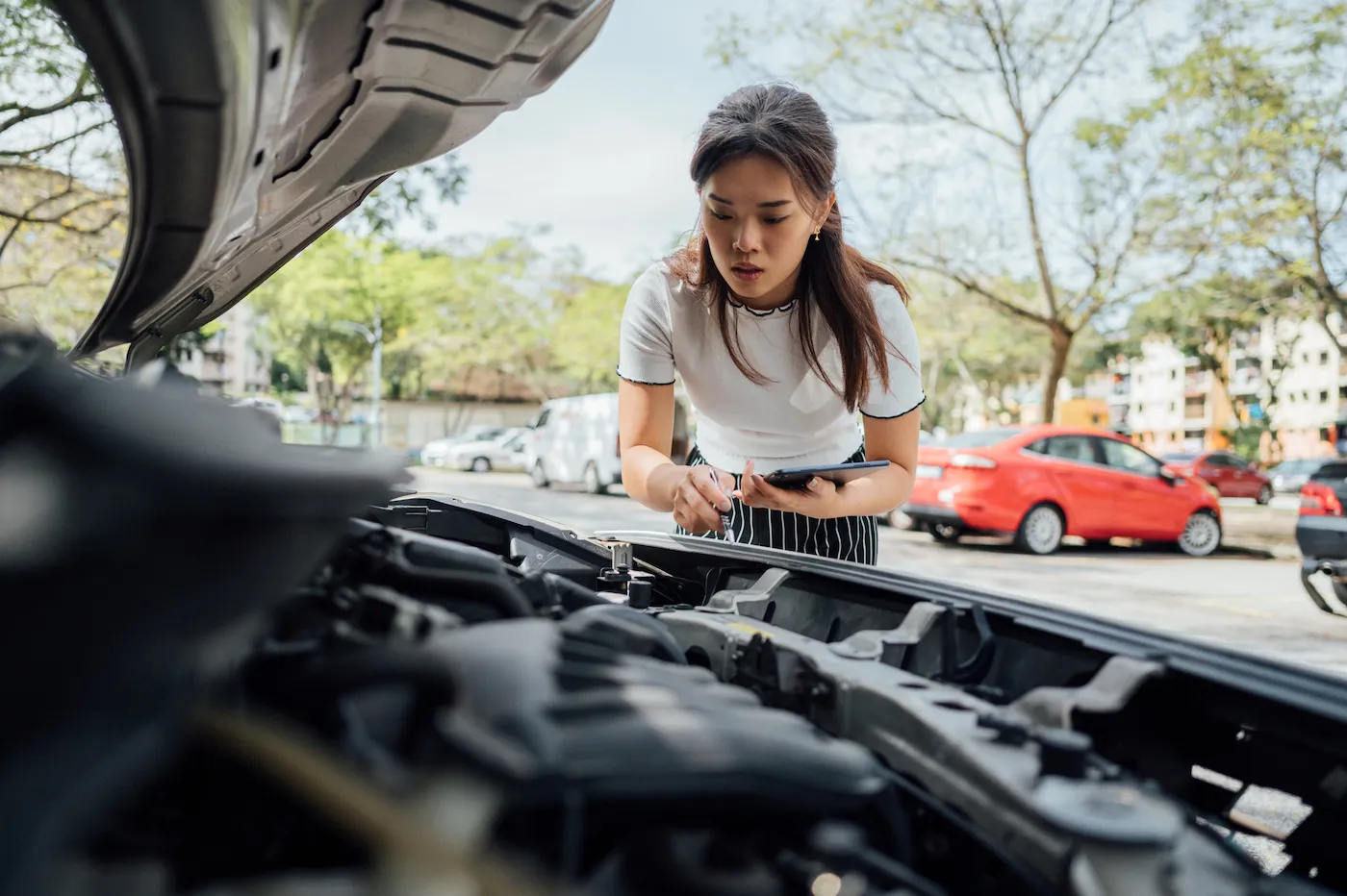 A woman holding a tablet assessing damage to a car after an accident