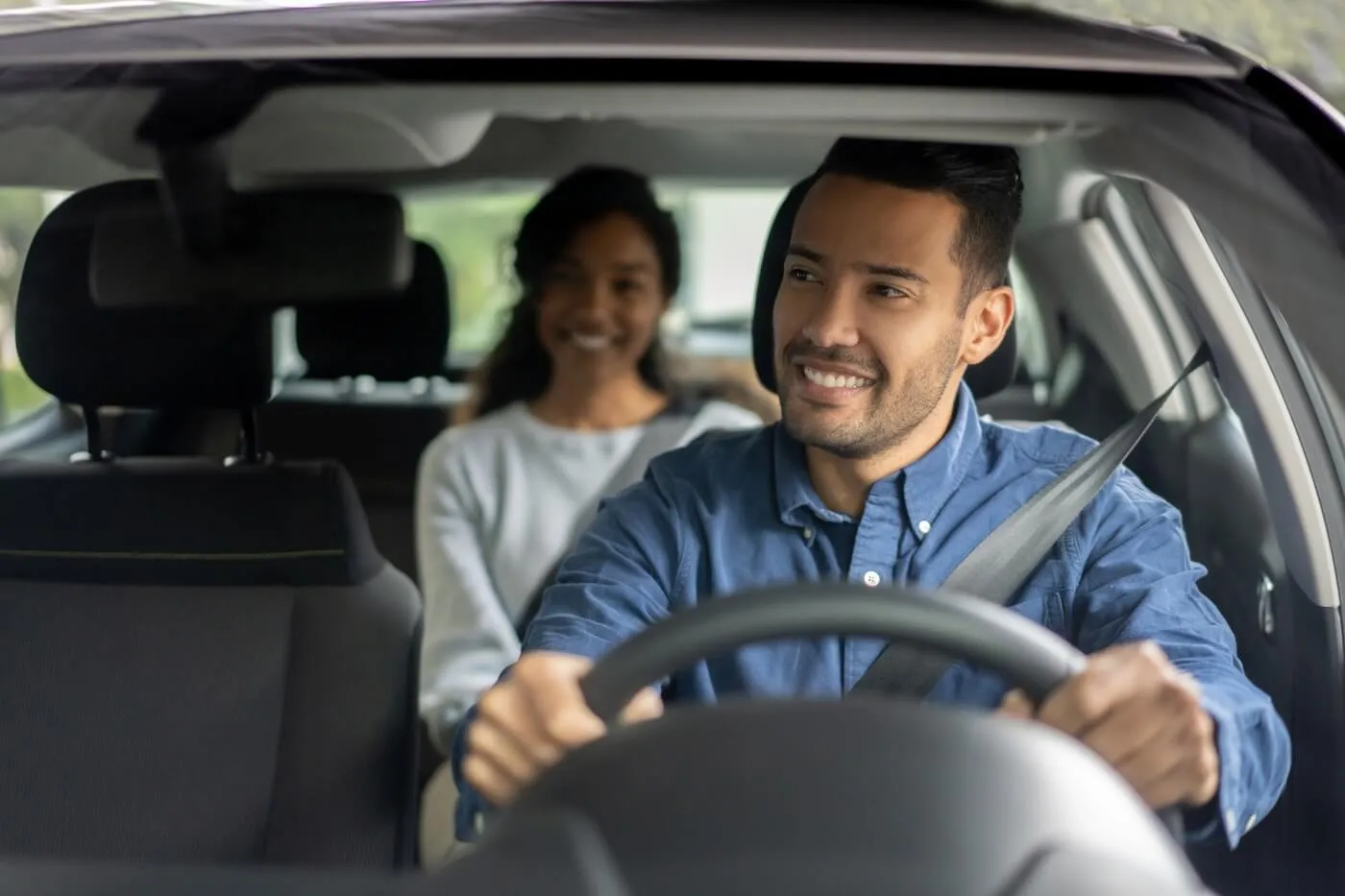 Smiling man driving a car with a female passenger on the back seat