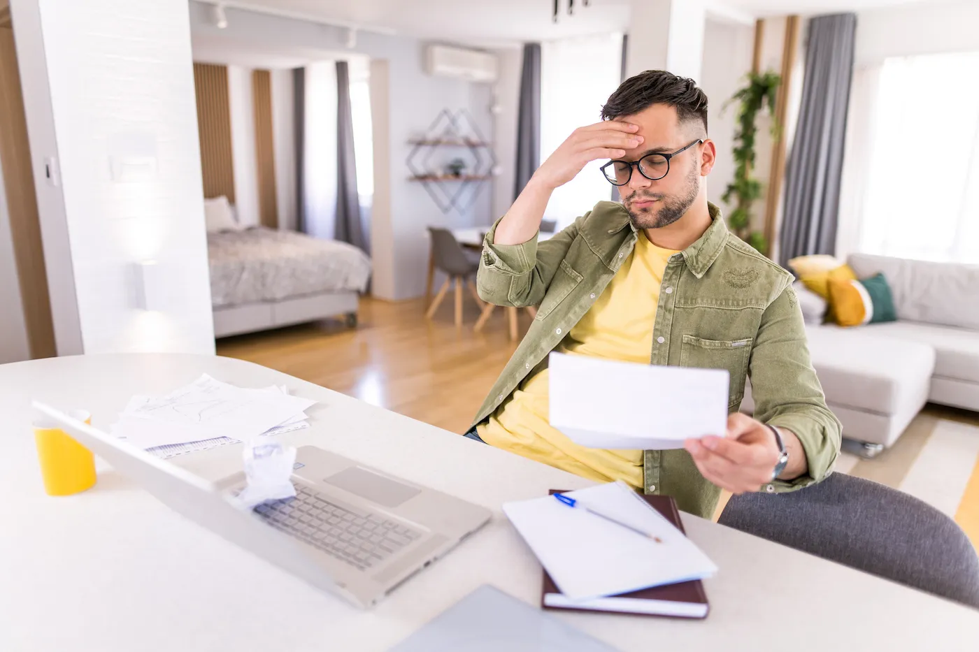 A college student avoiding student loan fees, looking concernedly at a paper while sitting at a desk in front of his laptop.