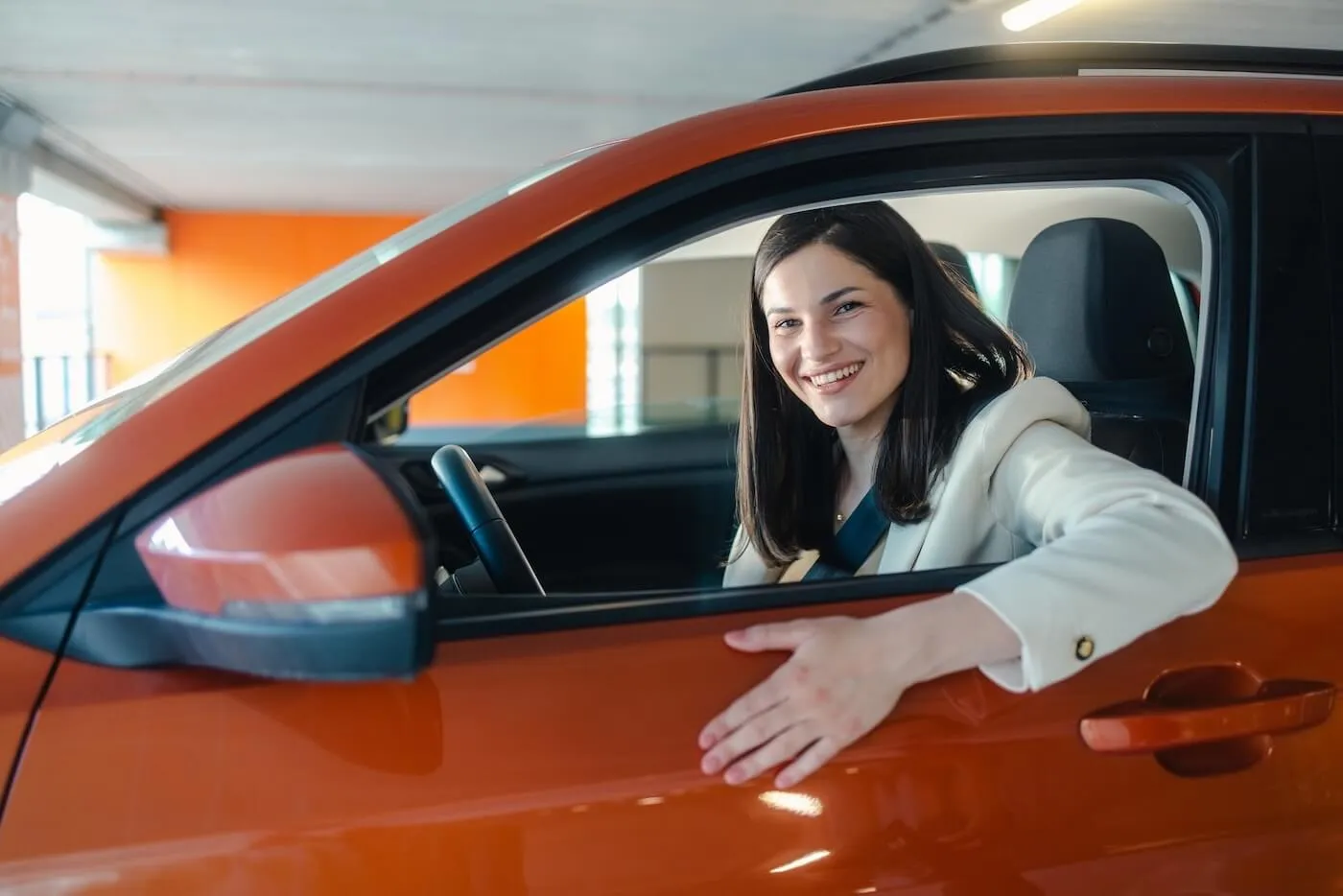 Smiling young woman sitting an orange car in a covered parking lot