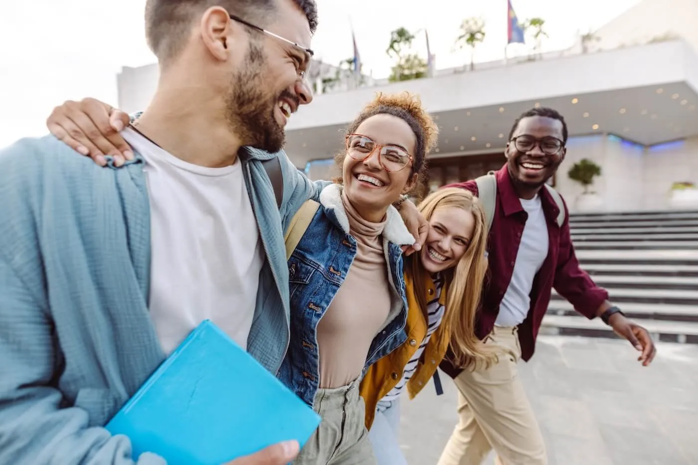 A group of four laughing students, males and females, are waling together in the campus