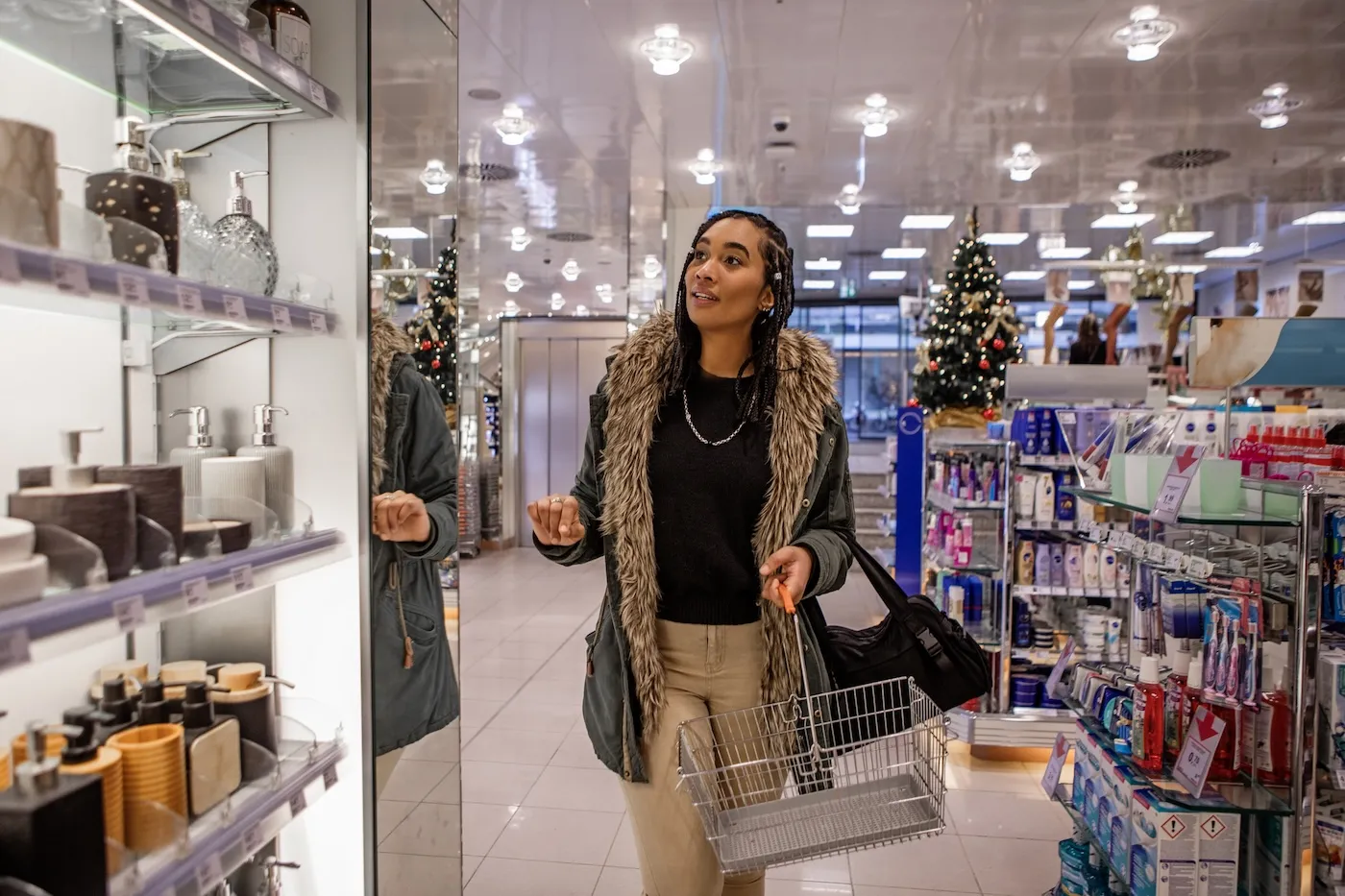 A woman holding a shopping basket and walking through a store with holiday displays.