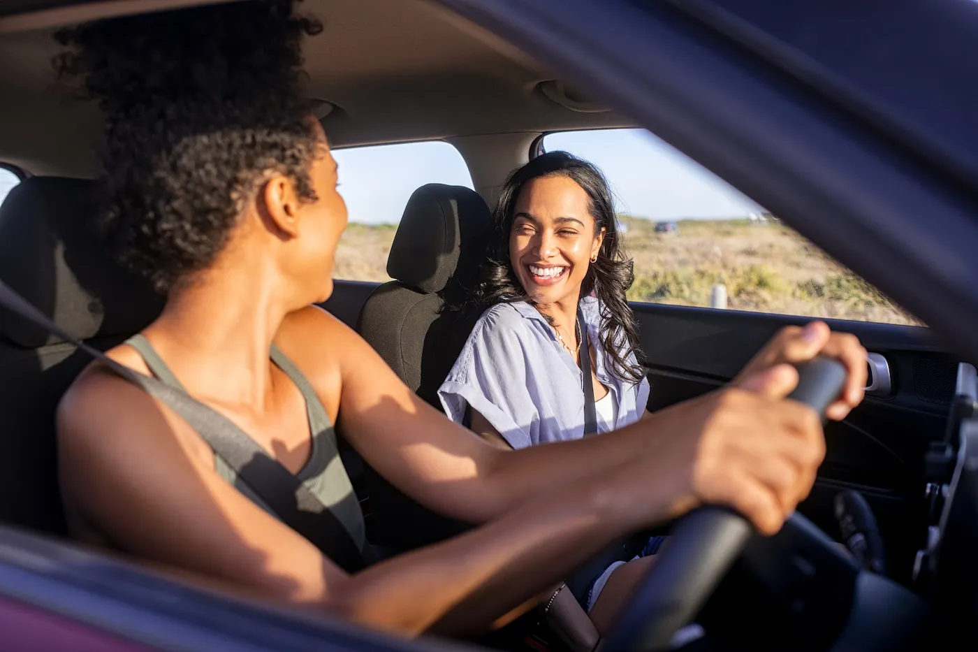 Happy laughing couple driving their shared car during sunset.