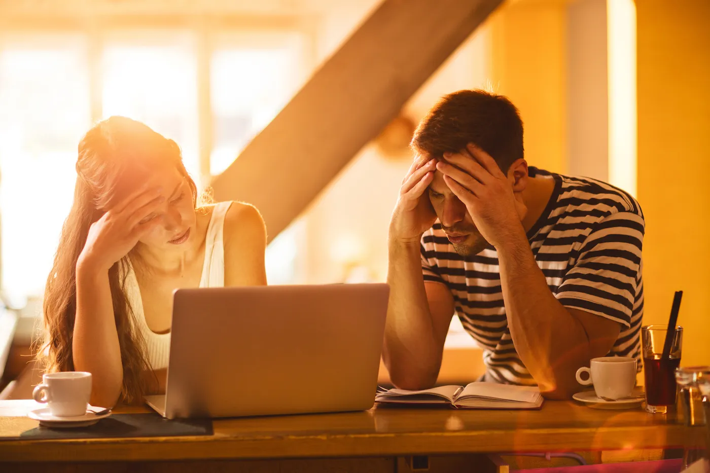 Stressed couple experiencing relationship difficulty while working on their finances at home during golden hour.