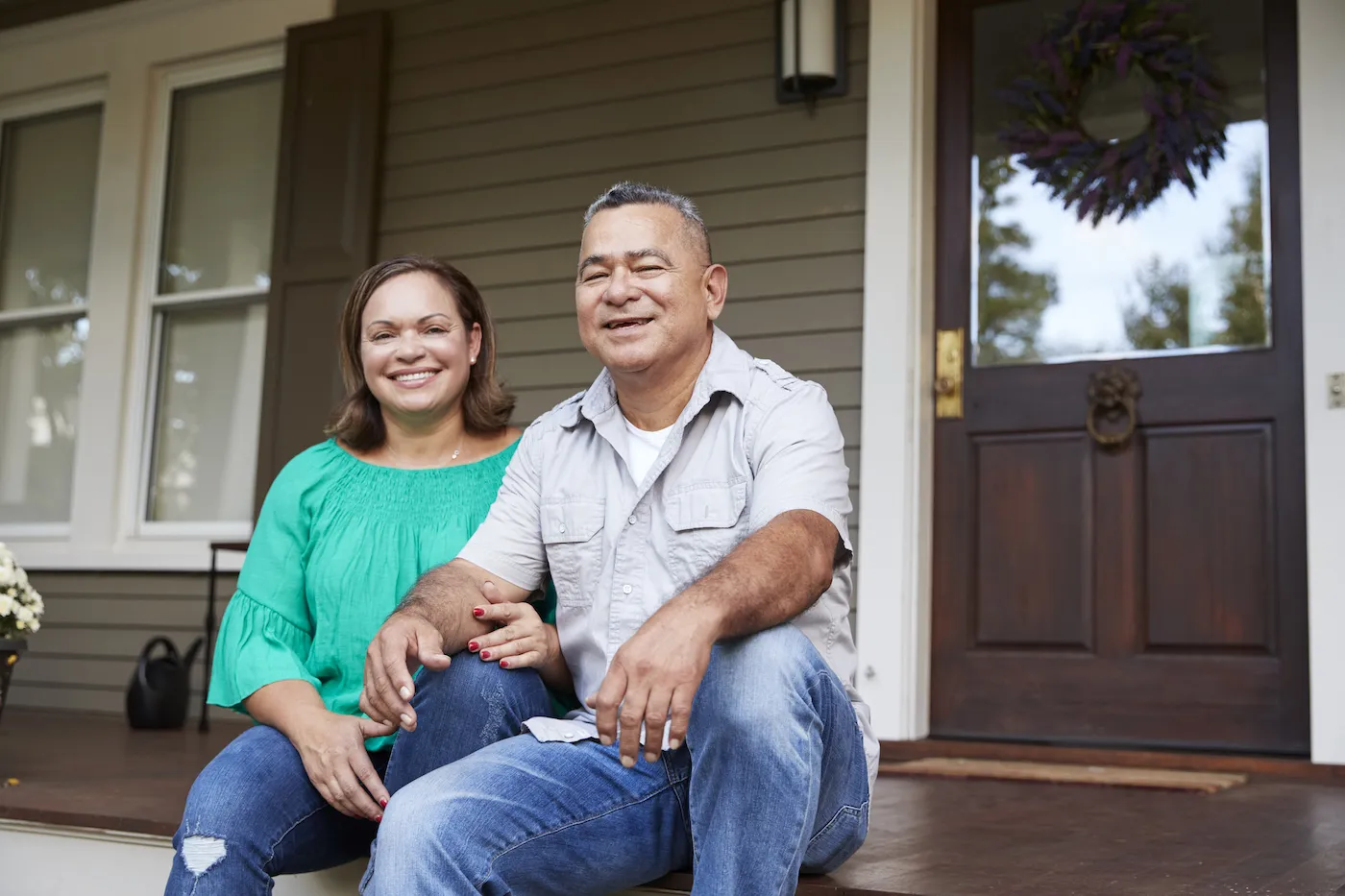 Portrait Of Smiling Senior Couple Sitting In Front Of Their Home