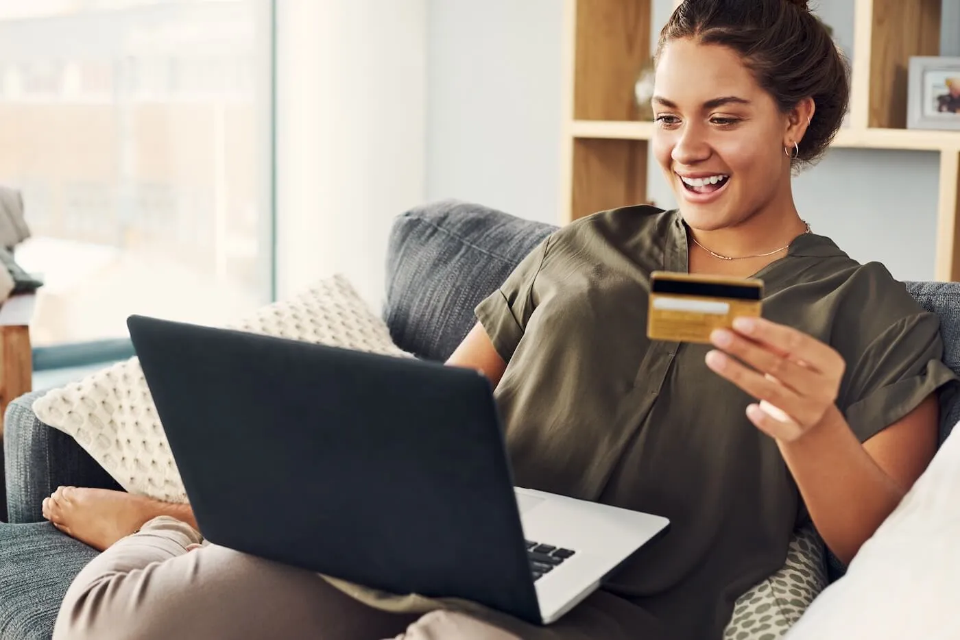 Smiling young woman uses her credit card for online shopping in her living room