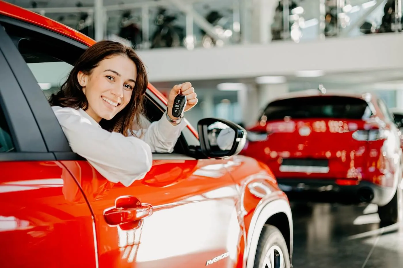 A smiling young woman sticks out of the red car window holding car keys