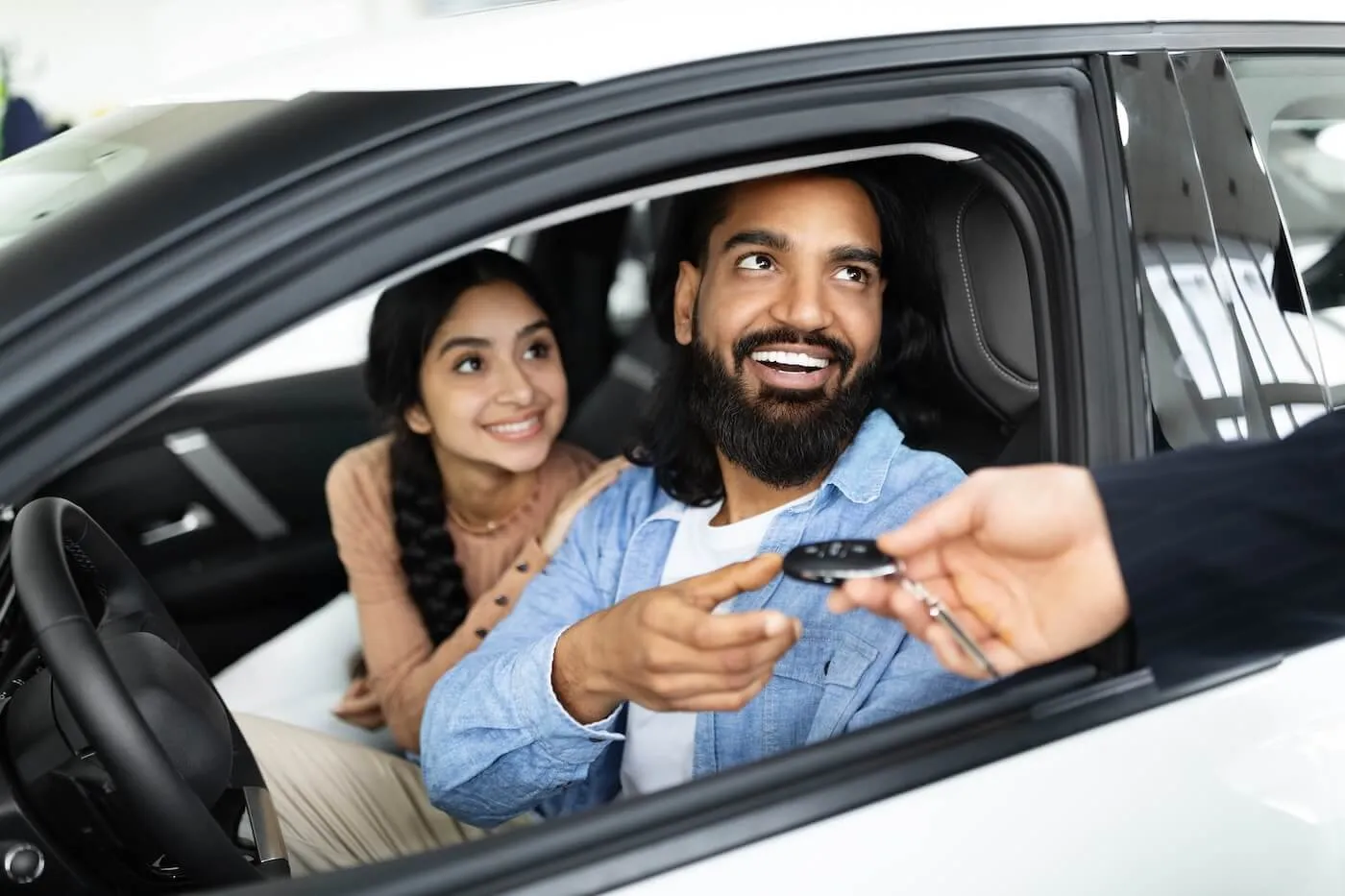 Happy couple sitting in the new car and taking the car keys from the agent