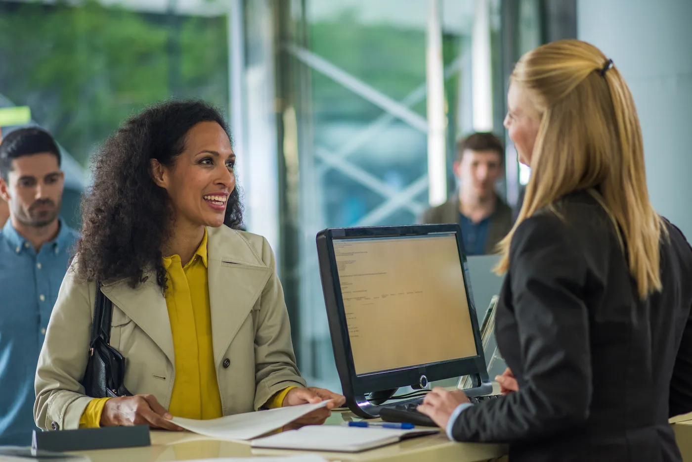 Customer holding document and smiling while bank teller helps them.