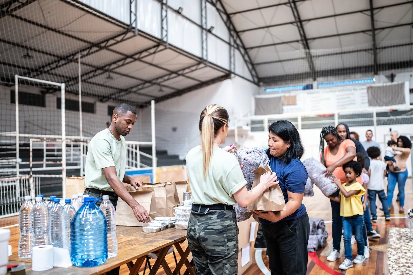 Soldiers giving donations to refugees at an aid station after a natural disaster.