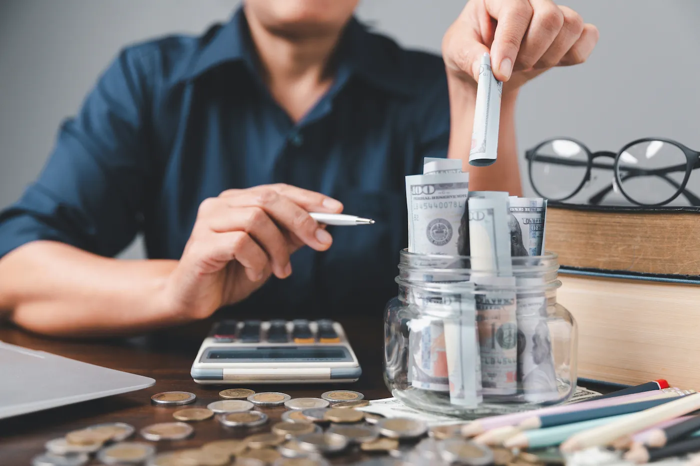 A person putting money into a full money jar, saving for debt