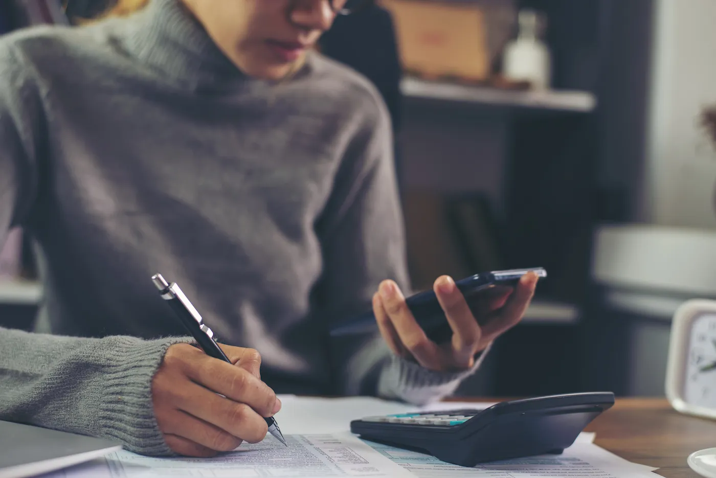 A person calculating expenses for checking accounts with a pen and paper and a calculator.