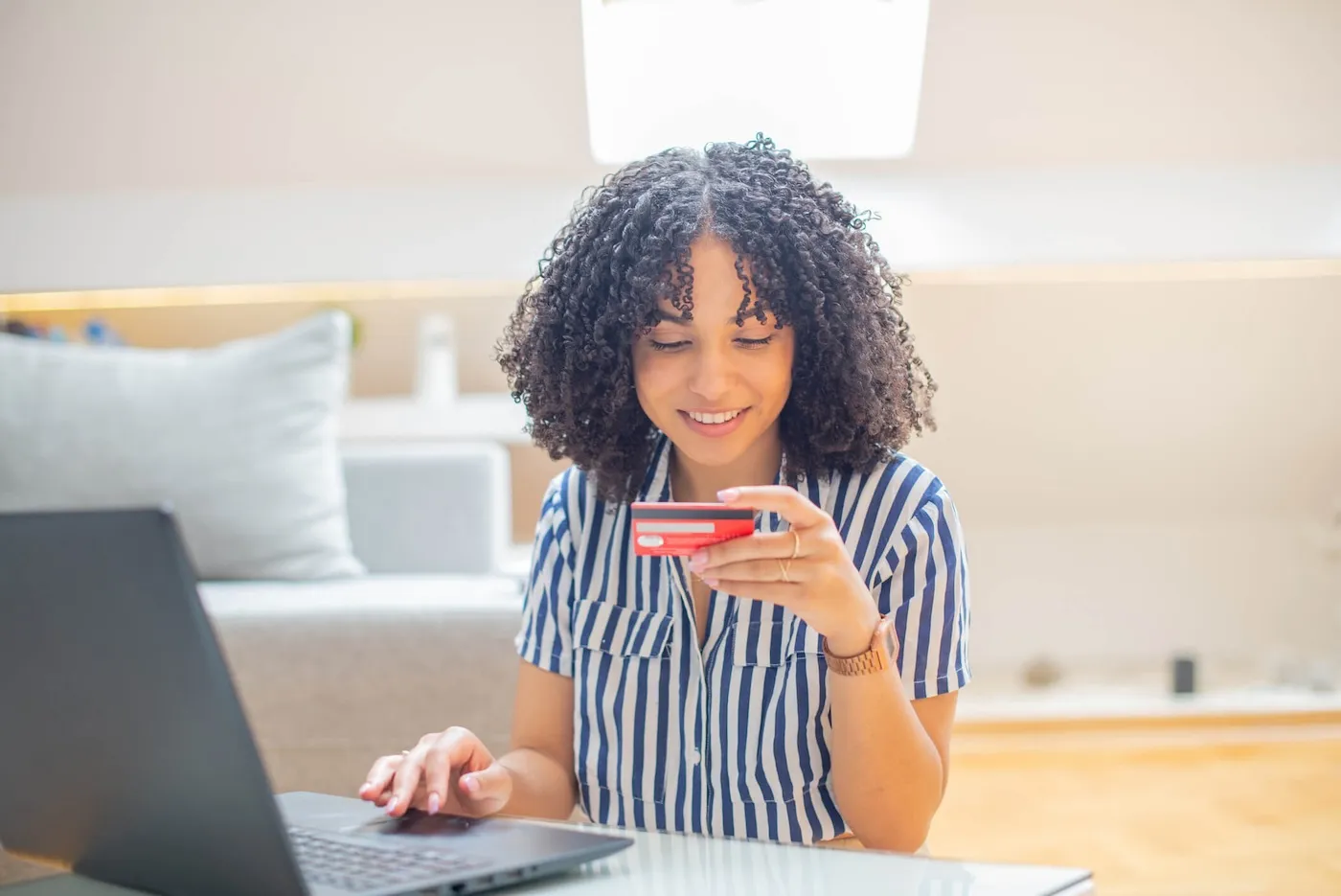 Smiling woman holding her credit card while using a laptop