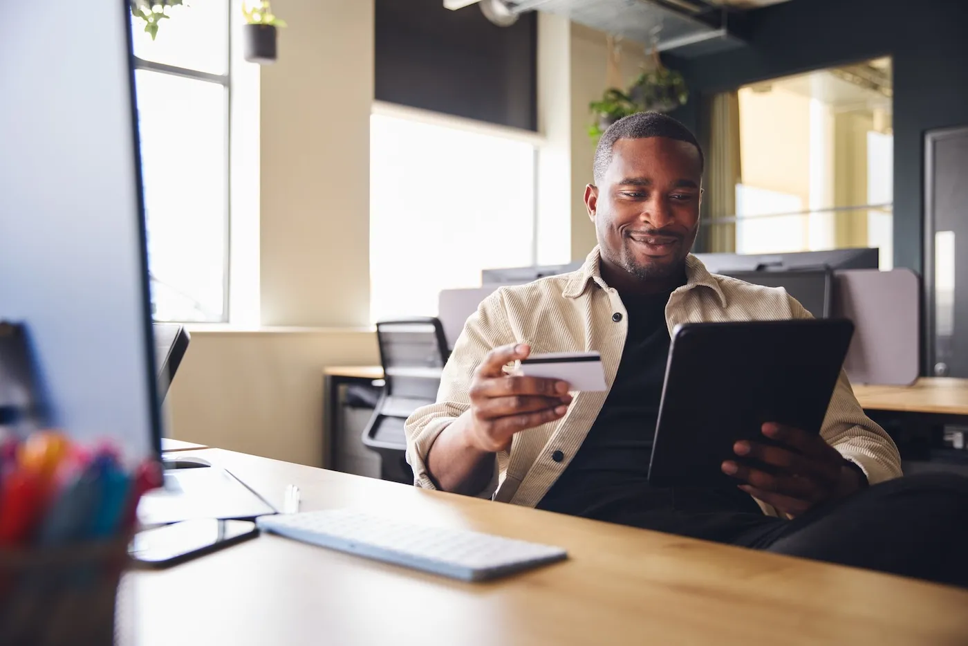 Smiling Man making online payment on tablet computer holding credit card in office.