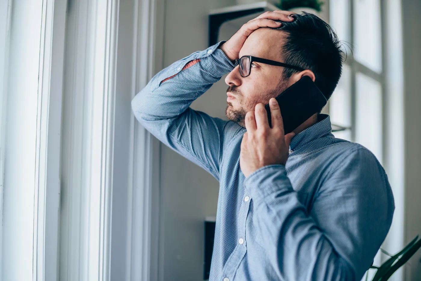 Worried man with hand on forehead talking on mobile phone in his office.