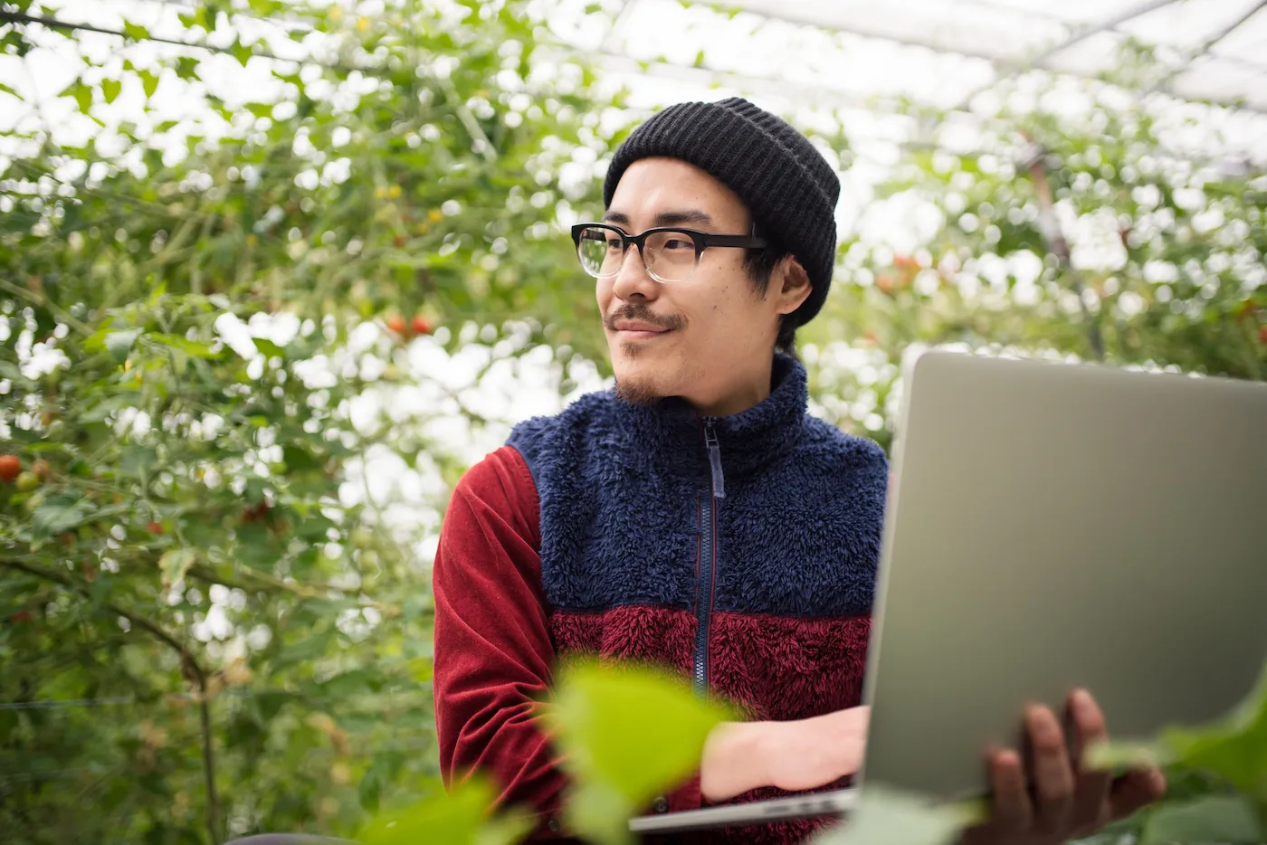 Young man with a laptop computer in a greenhouse conducting research.