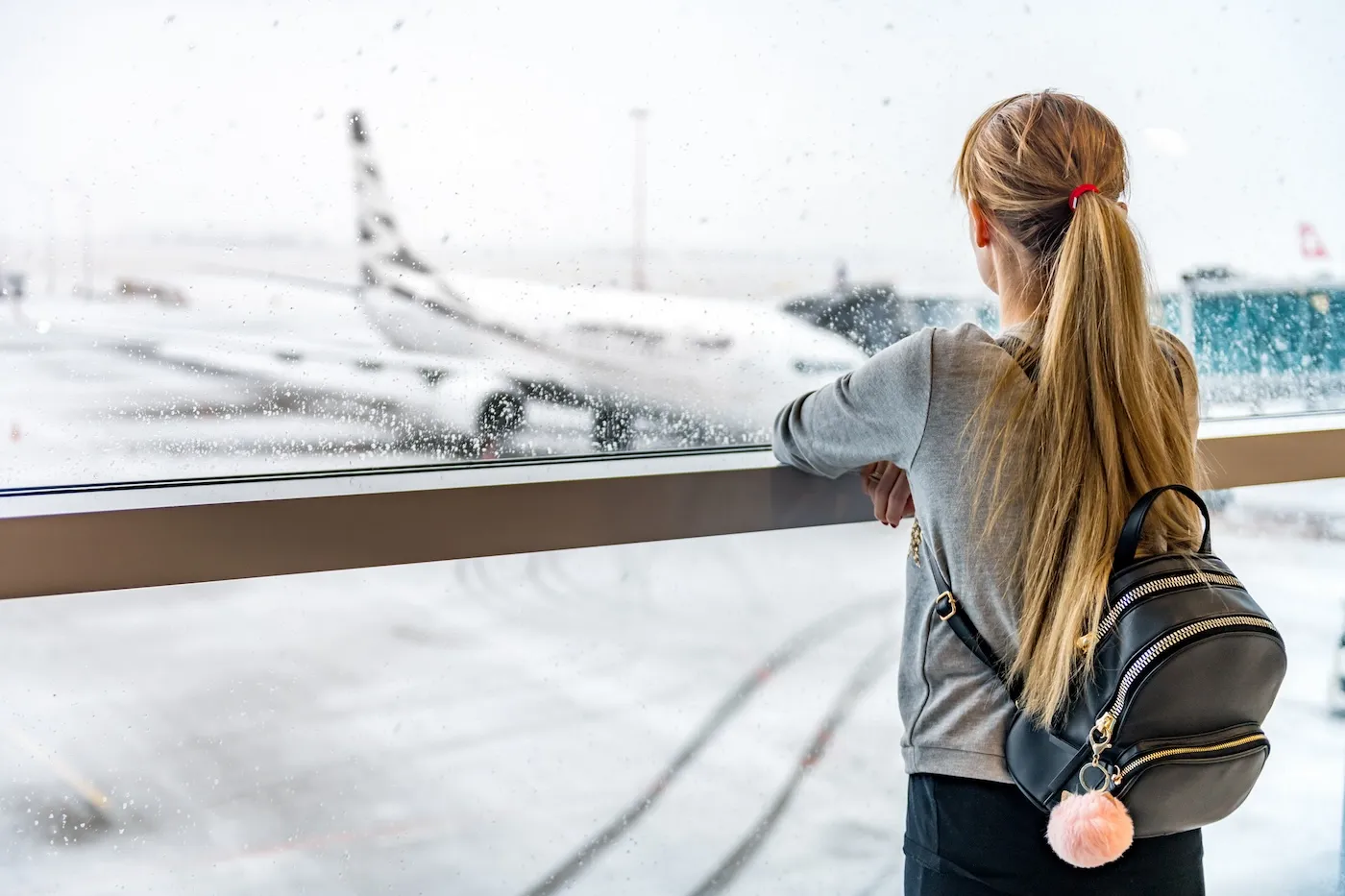 Horizontal color image of airplane during snowstorm and woman looking and waiting for departure.